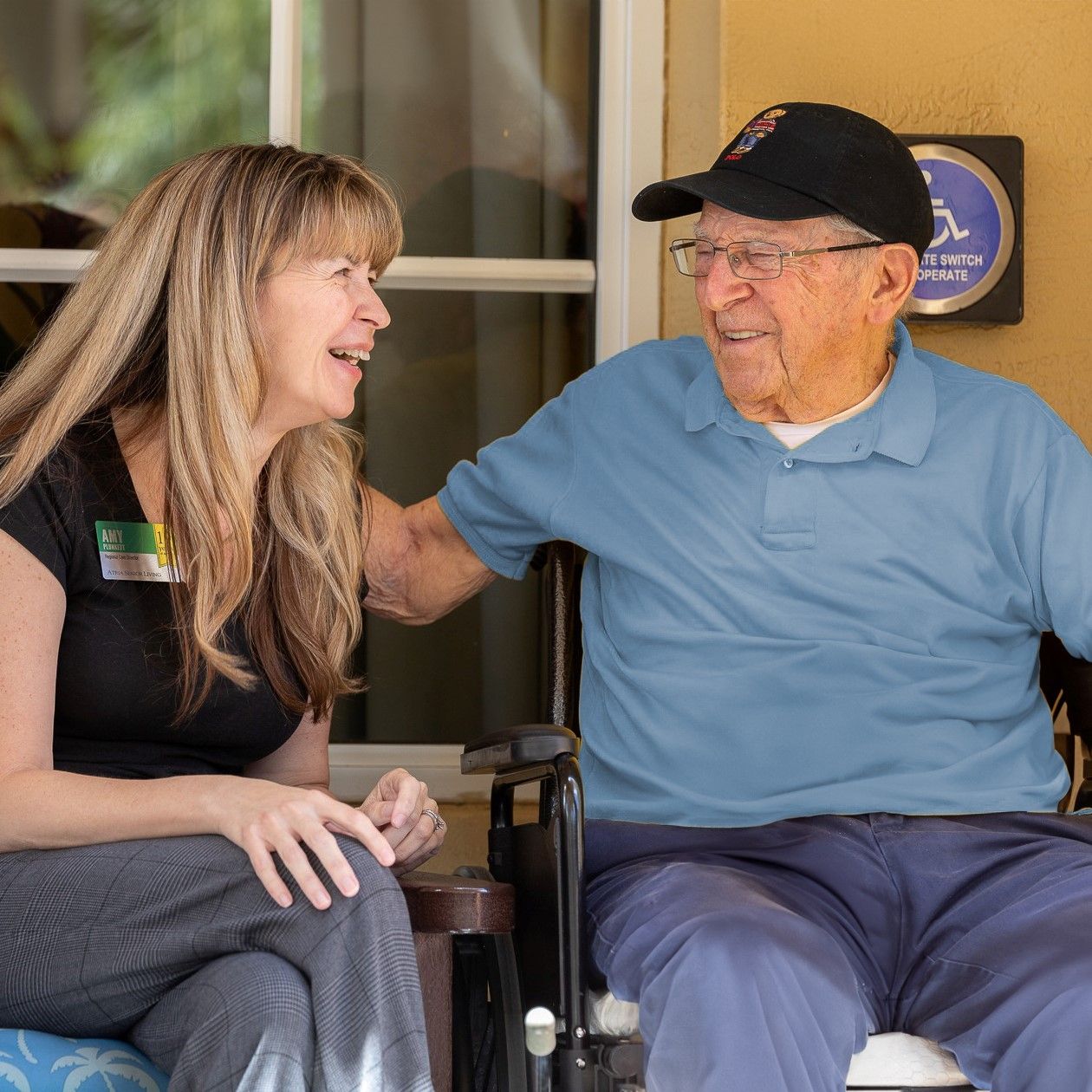 Older man and Atria staff member sit and laugh outside community building
