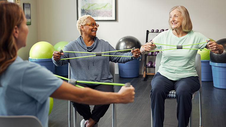 Two senior women sitting and stretching with an exercise band