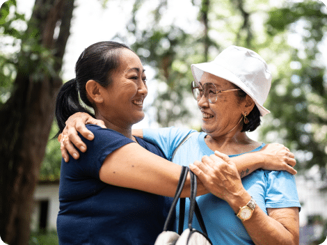 Senior resident and daughter hugging outdoors, trees in background.