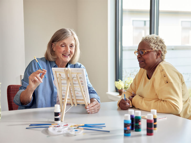 Two senior women painting a canvas together
