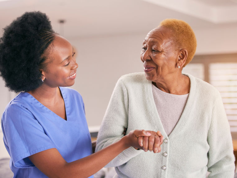 An older woman gets escorted by a younger woman wearing scrubs