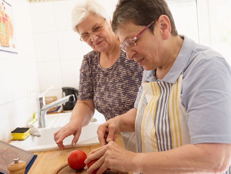 Two senior woman cutting a tomato and preparing for a meal