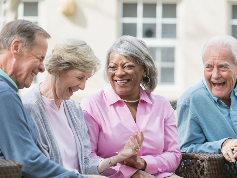 Two senior couples sitting together laughing on the bench