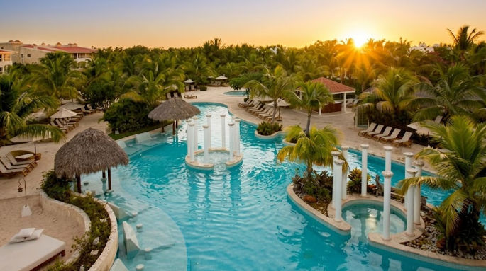 Beautiful lagoon-style swimming pool with white columns and palm trees at sunset at The Level at Melia Caribe Beach, Punta Cana