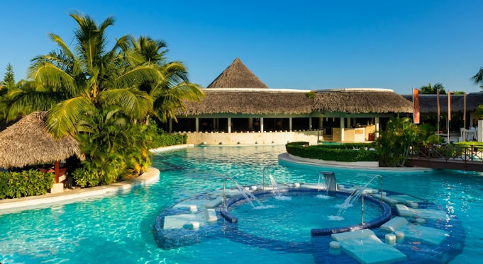 Lujosa piscina con chorros de agua, tumbonas sumergidas y palmeras en The Reserve at Paradisus Punta Cana Resort