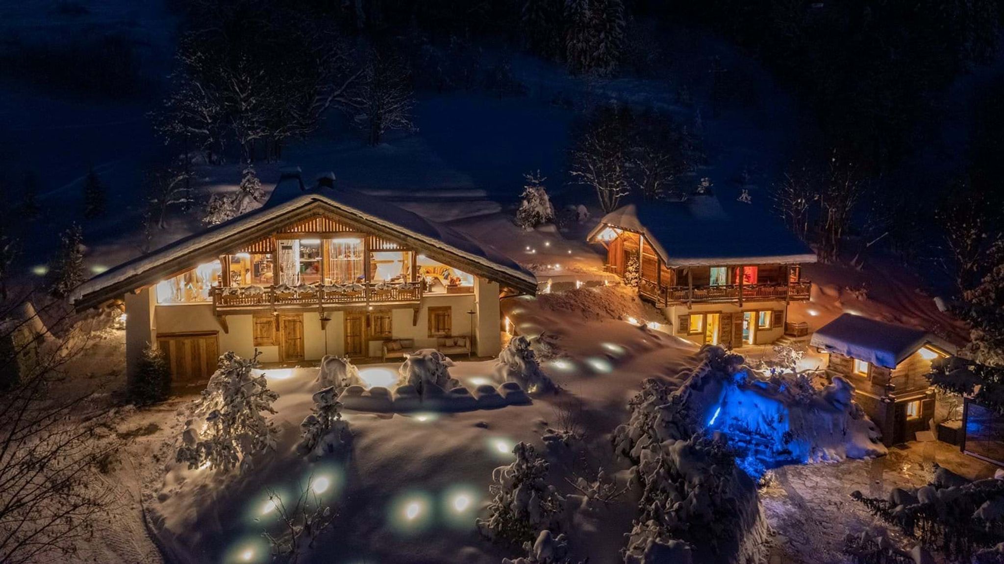 Chalet exterior at night with separate guest cabin and illuminated grounds