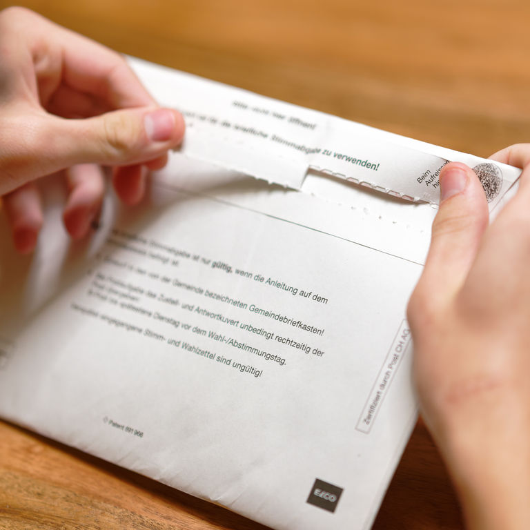 Zwei Hände öffnen ein Abstimmungskuvert