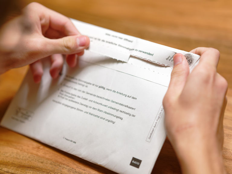 Zwei Hände öffnen ein Abstimmungskuvert Zwei Hände öffnen ein Abstimmungskuvert