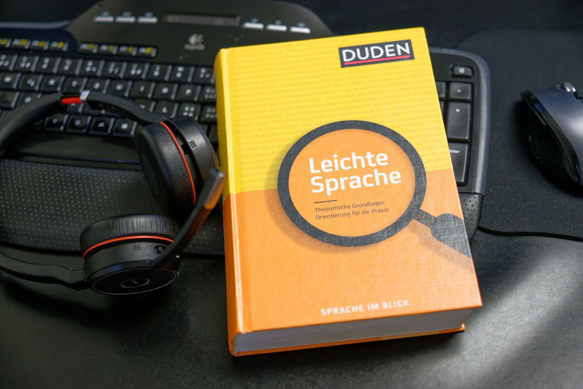 Das Buch zur Leichten Sprache aus dem Duden-Verlag liegt neben einem Headset auf einer Tastatur.