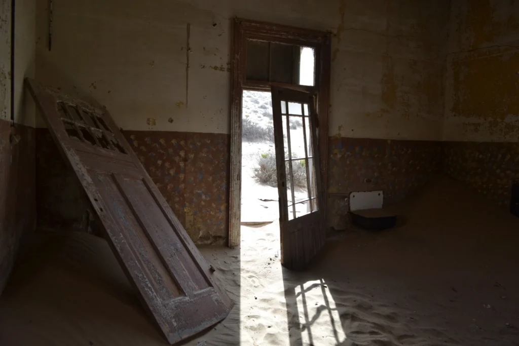 Dark abandoned interior at Kolmanskop with broken doors and sand on the floor