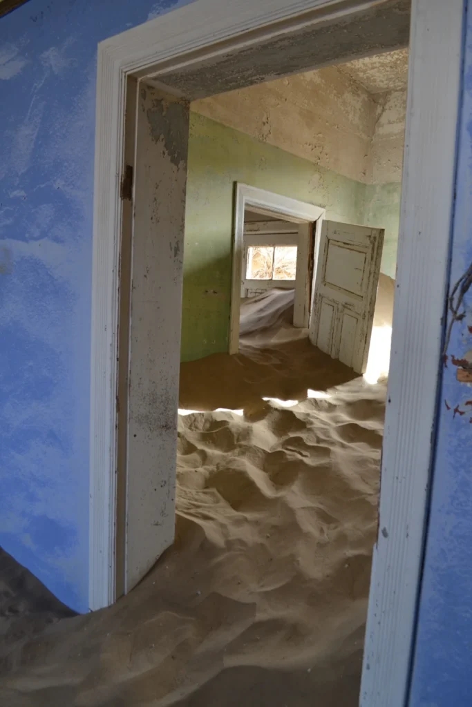 Blue painted room looking through doors into sand-filled rooms at Kolmanskop Namibia