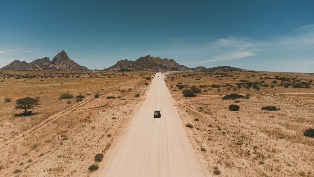 Vehicle travelling along a remote road toward mountains at Spitzkoppe, Namibia