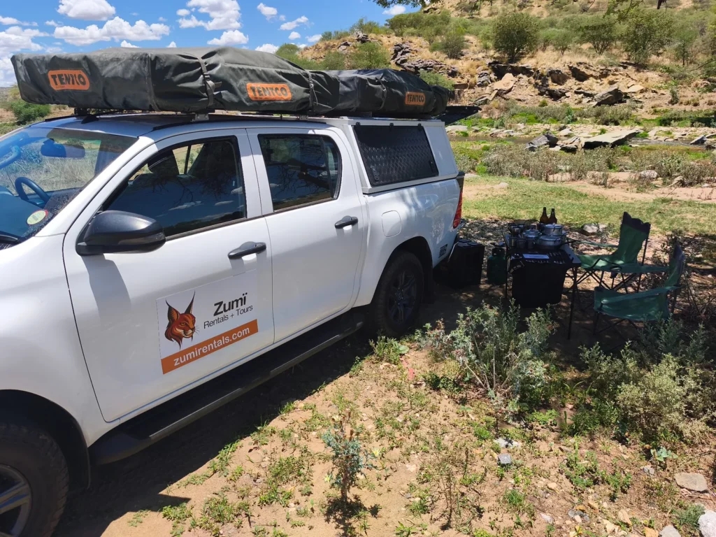 Zumi Toyota Hilux with rooftop tents and camping equipment set up beside a river in Namibia