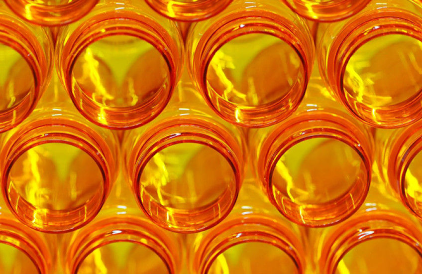 A close-up view of stacked, translucent orange glass jars, creating a geometric pattern with light reflections.