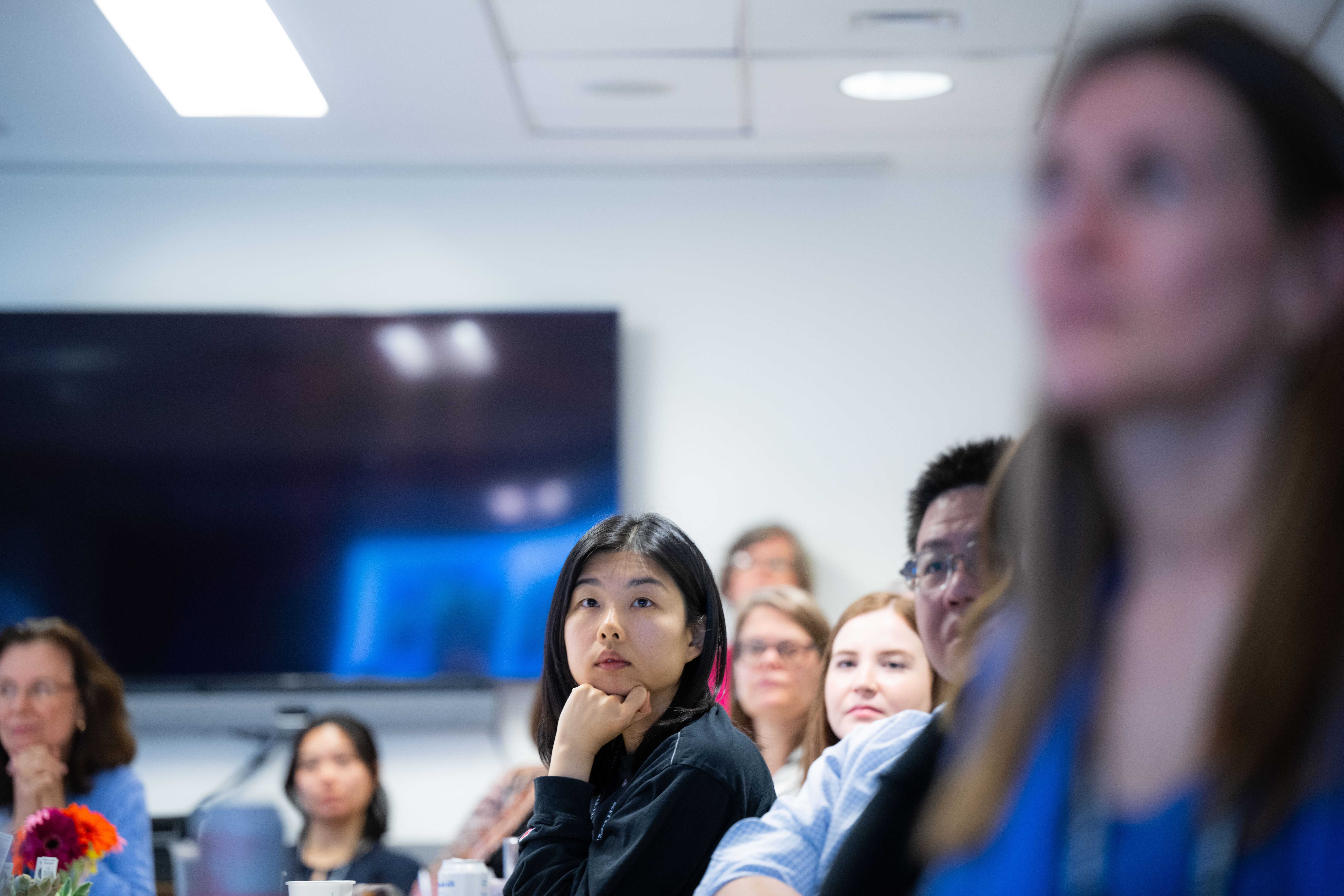 A group of HMS students at a seminar, focused and engaged, with a woman in the foreground appearing thoughtful.