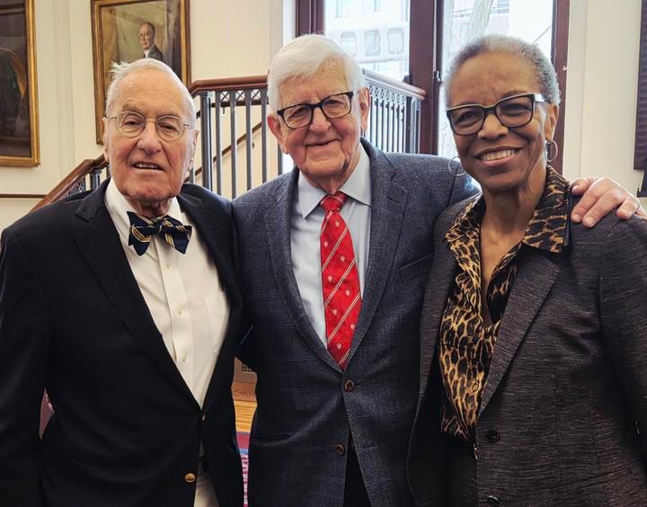 Dr. Frederick H. Lovejoy, former HMS Dean Dr. Joseph B. Martin, and Dr. Joan Reede standing together, smiling, indoors with a staircase and portraits in the background.