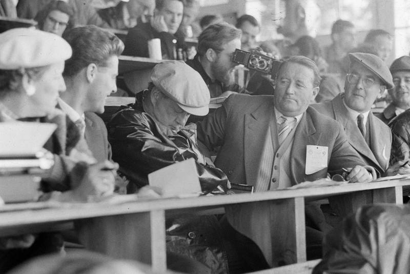 A journalist falls asleep in the press box. Denis Jenkinson can be seen checking a camera just behind.