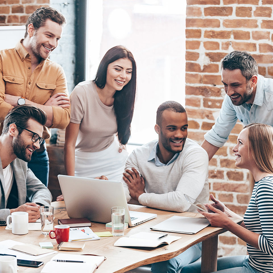 Group of cheerful young people discussing something with smile and gesturing while leaning to the table in office