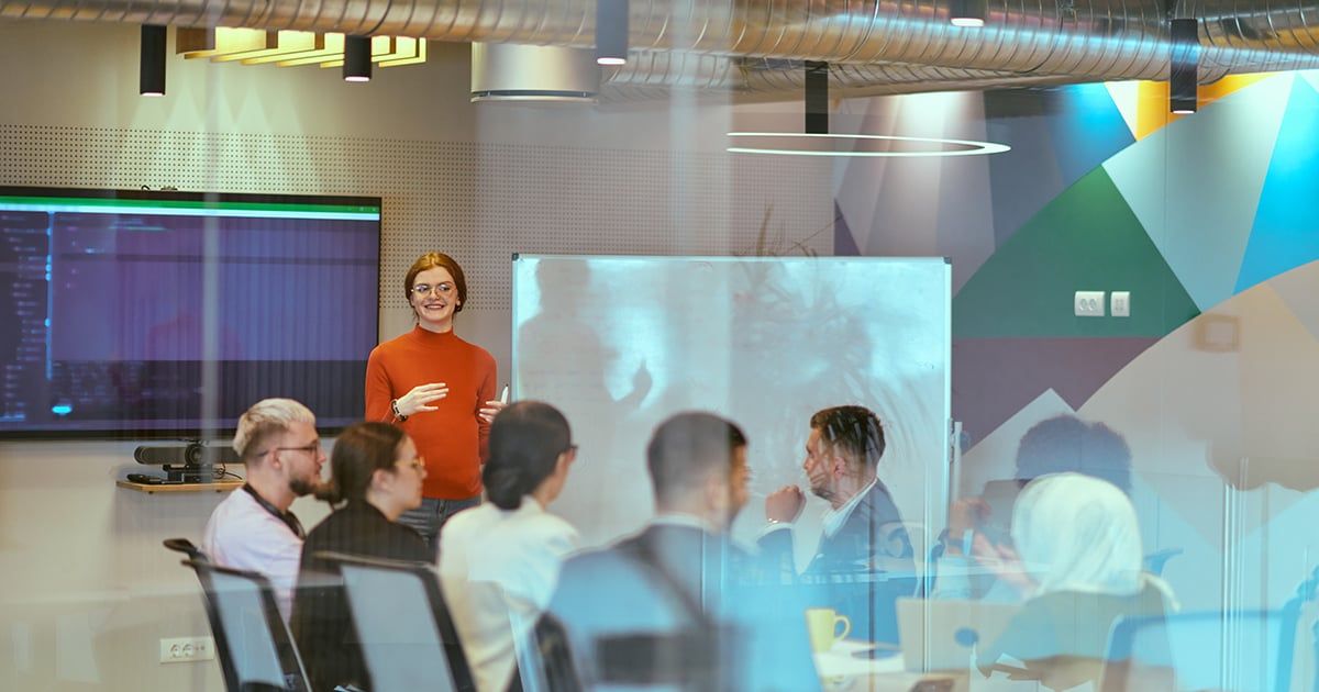 A pregnant business woman with orange hair confidently presents her business plan to colleagues in a modern glass office, embodying entrepreneurship and innovation.